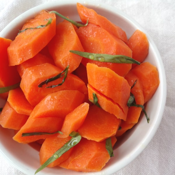 A white bowl filled with carrots, topped with tarragon and honey sitting on top of a white towel