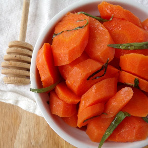A white bowl with cooked carrots drizzled with honey and topped with fresh chopped tarragon.