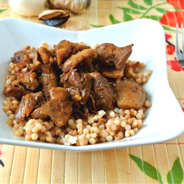 Chicken thighs made in an electric skillet on top of large toasted couscous.