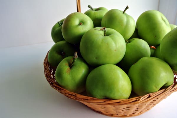 A brown basket full of green Transparent Apples