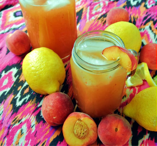 Homemade Peach Lemonade in jar glasses surrounded by peaches and lemons. 