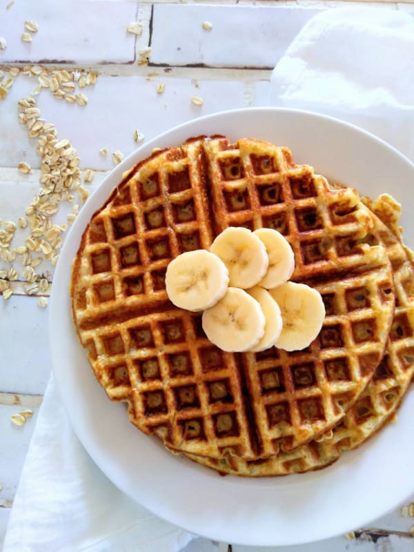 Alton Brown's Oat Waffles stacked in a white dish. There are slices on bananas on top of the waffles.