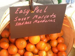 A small basket of mandarins with a sign that says "Easy Peel Sweet Murrcots Seedless Mandarins"