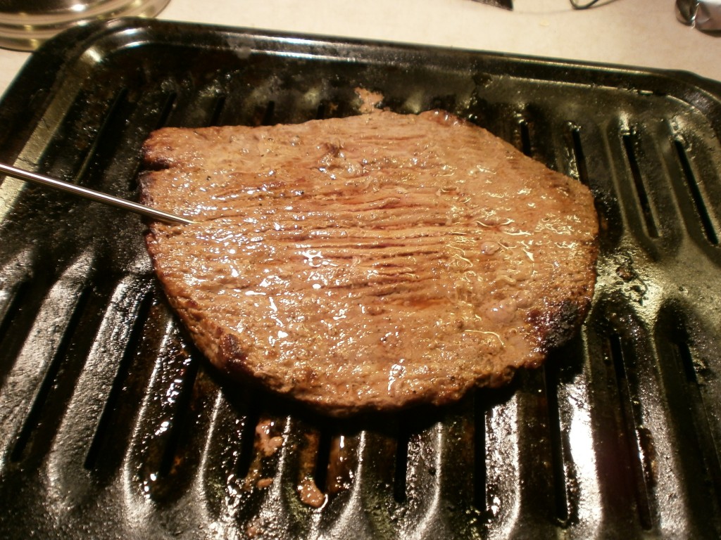 A cooked Flank steak on a  black broiler pan 