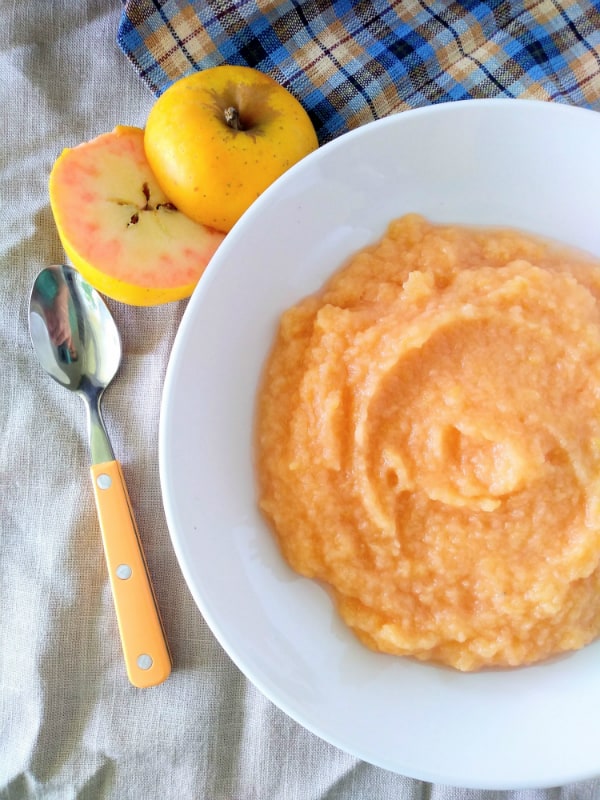 A rosy colored applesauce in a white bowl. The applesauce was made with Pink Pearl apples which sit next to the bowl.