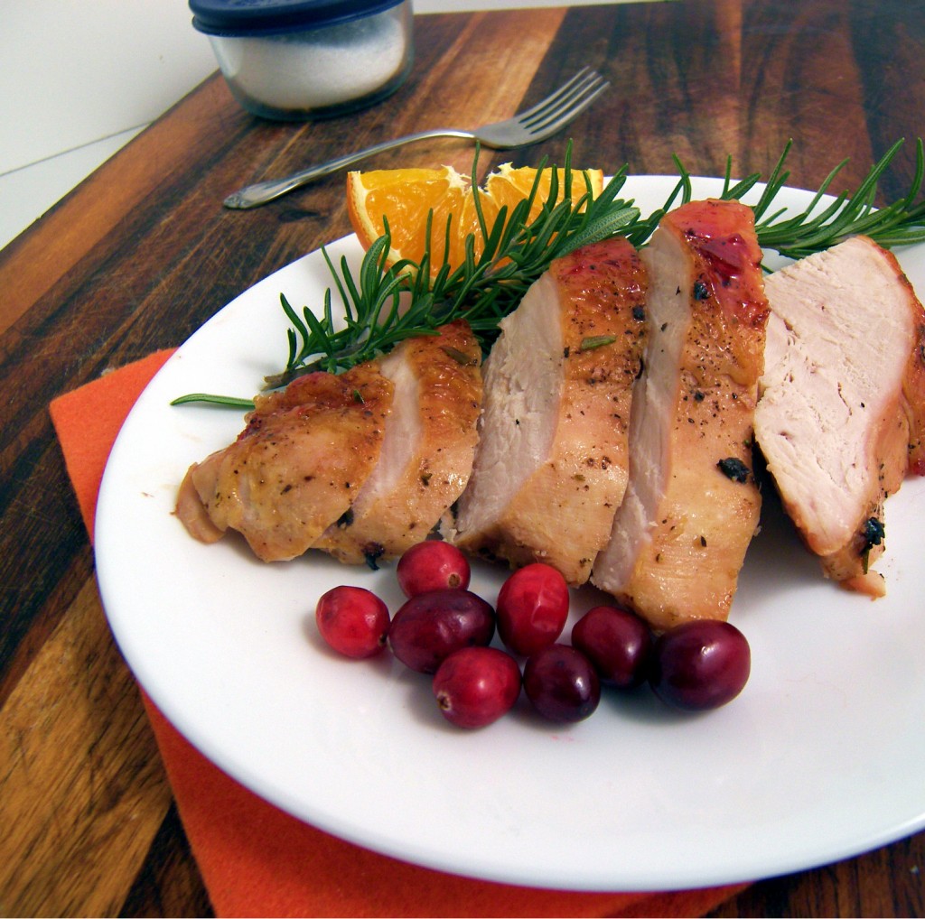 Sliced up pieces of turkey breast on a white plate with a slice of orange, rosemary, and cranberries