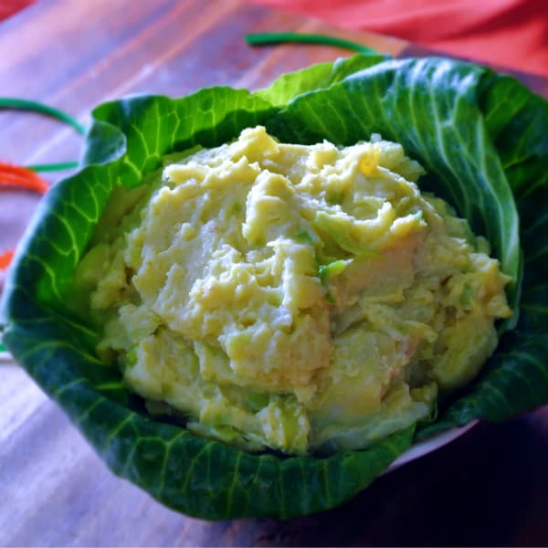 Irish Colcannon potatoes with cabbage inside of cabbage leaves on a wood board with orange and green ribbon on it.