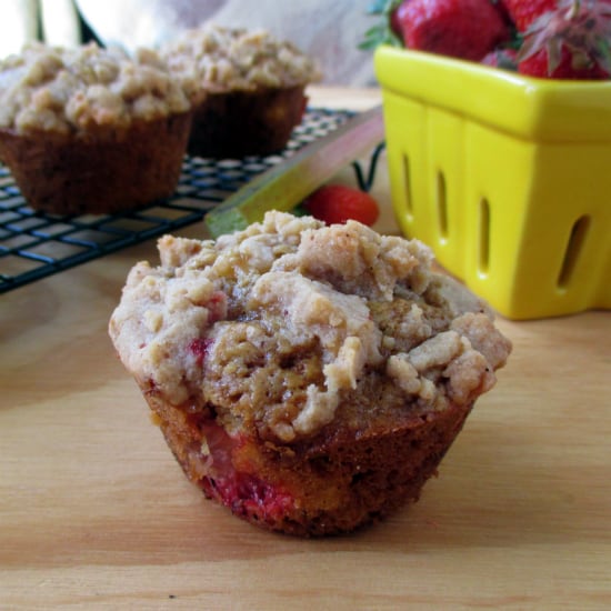 Strawberry Rhubarb Muffins with one sitting on a wood board and other ones cooking on a drying rack.