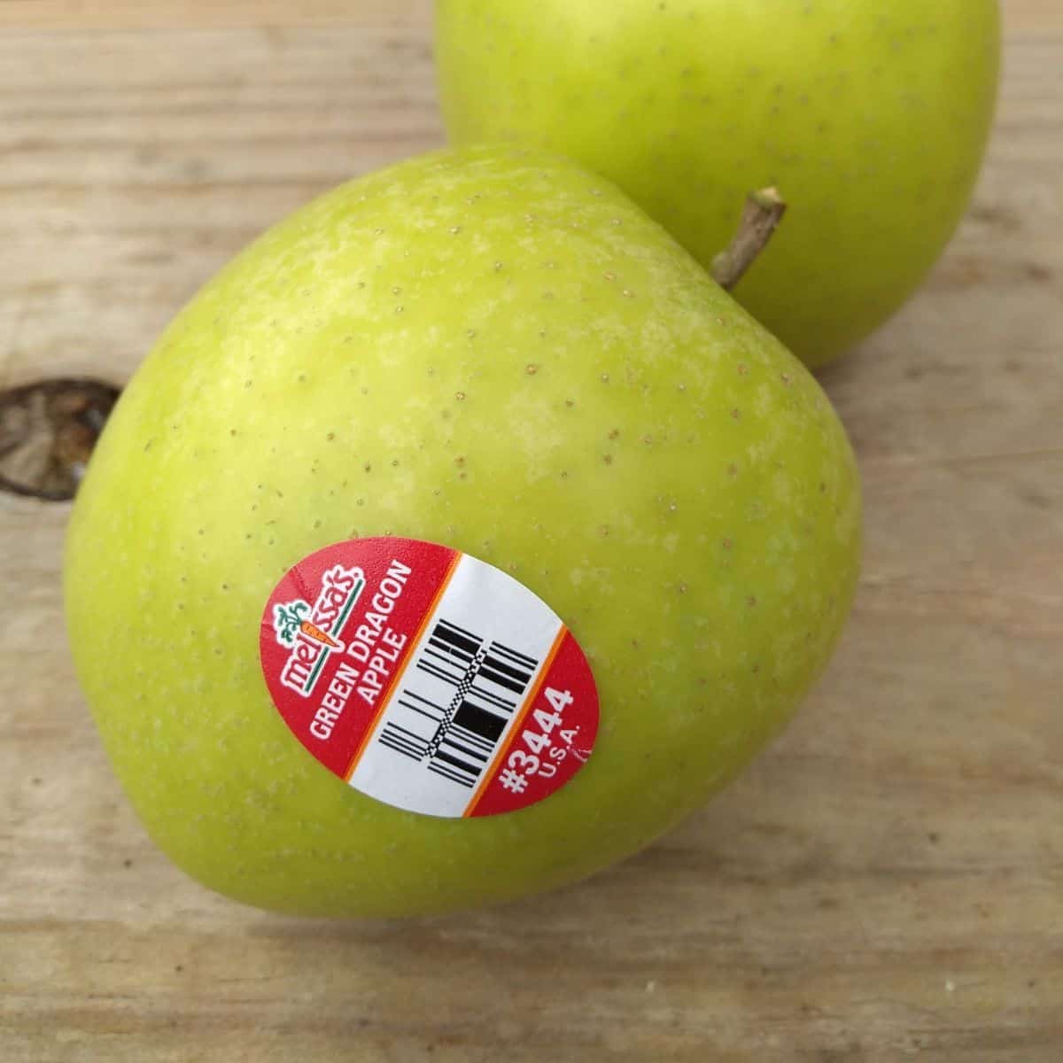 A Green Dragon apple with the sticker on it sitting on a wood table.
