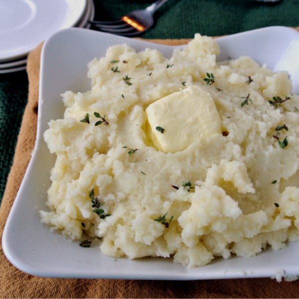 Mashed potatoes with a pat of butter on top in a square shaped bowl.