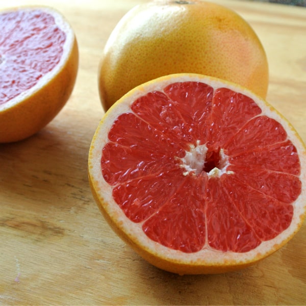 A sliced up red Texas grapefruit sitting on a wood board.