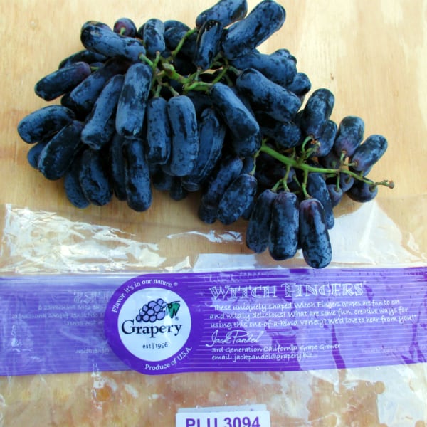 Elongated black grapes on a wood board with a bag that says Witch Fingers