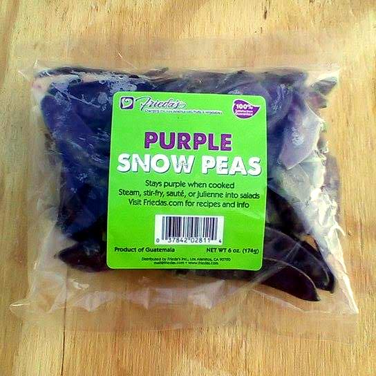 A plastic bag of Frieda's Purple Snow Peas on a wood board.