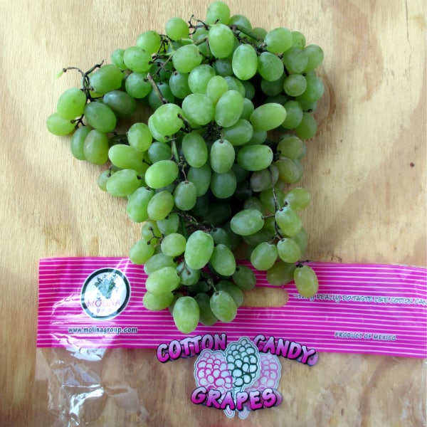 A bunch Cotton Candy Grapes from Mexico sitting on a wood board with  the empty grape bag.