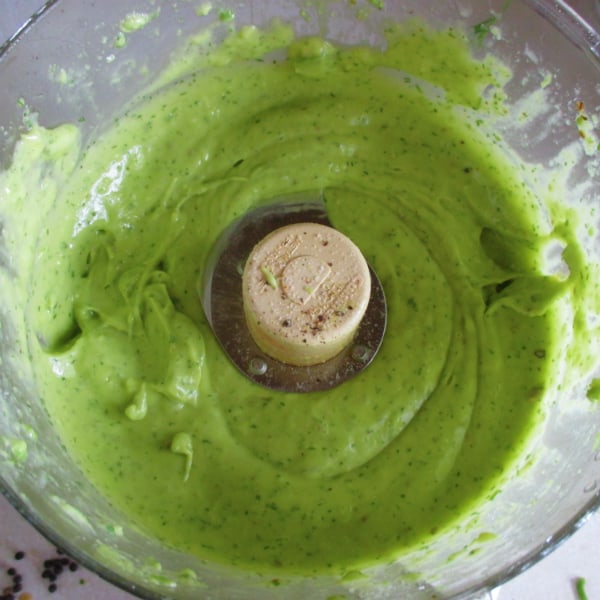 Prepared Avocado Dressing in the work bowl of a food processor with the blade still in the bowl.