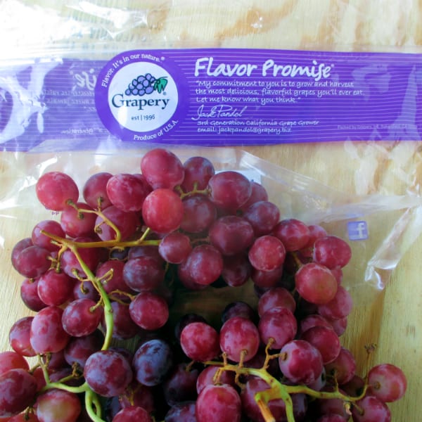 An old Grapery Flavor Promise bag on a wood board with the red grapes on top of the bag