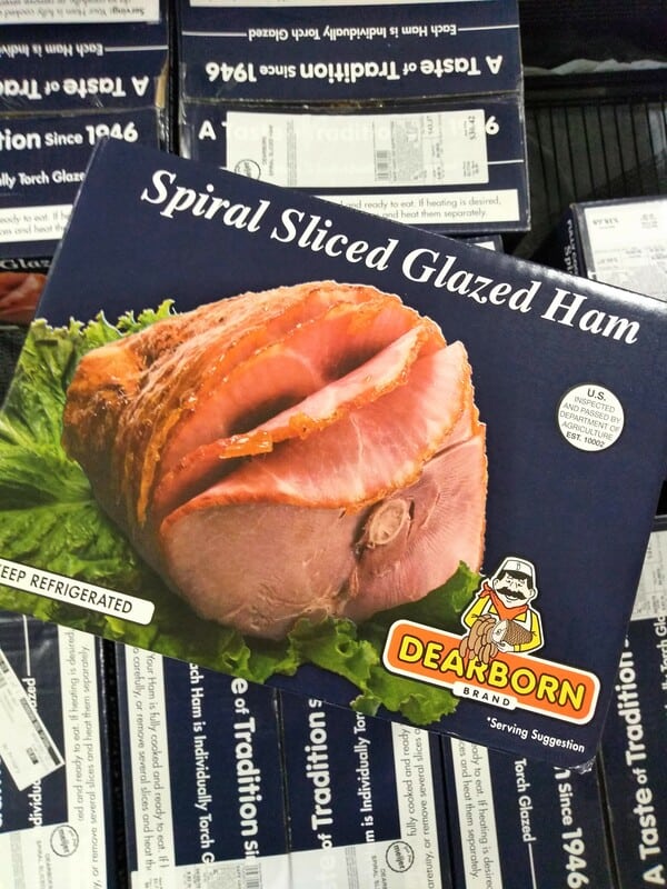 A blue box Dearborn brand Spiral Sliced Glazed Ham on top of other boxes at the grocery store.