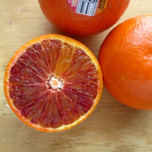 Three Ruby tango mandarins on a wood board with one of them sliced open to show the red interior. 