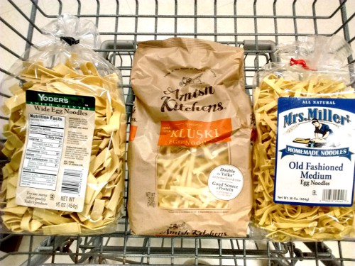 Three bags of egg noodles in a shopping cart. From left to right, Yoder's Wide Egg Noodles, Amish Kitchens noodles and Mrs. Miller Old Fashioned Medium egg noodles.