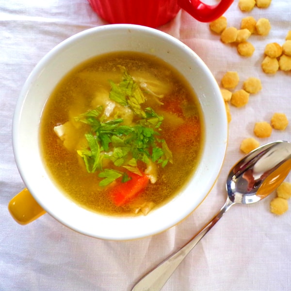 A soup mug filled with chicken noodle soup on a white towel with a soup and oyster crackers next to it.