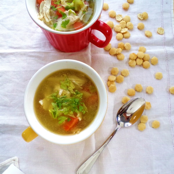 Two large soup mugs on a white towel with oyster crackers surrounding them.