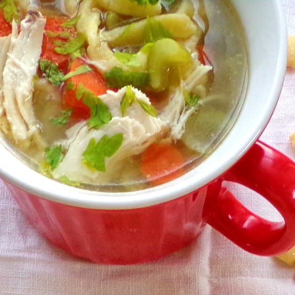 A red soup mug full of chicken noodle soup sitting on a white towel.