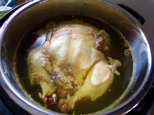 A Whole cooked Chicken sitting in an opened Instant Pot with liquid.