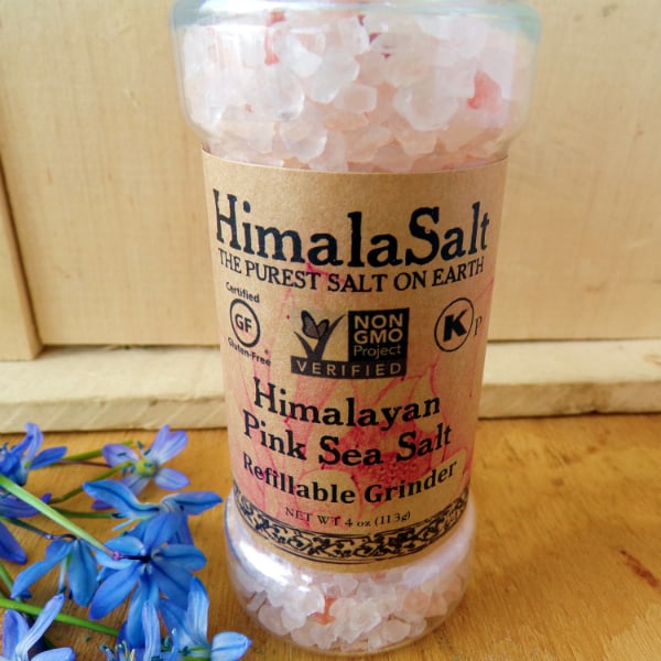 A grinder of Himala Salt Himalaya Pink Sea Salt in front of a wood board.