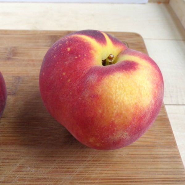 A single Blaze Prince peach sitting on a wood cutting board