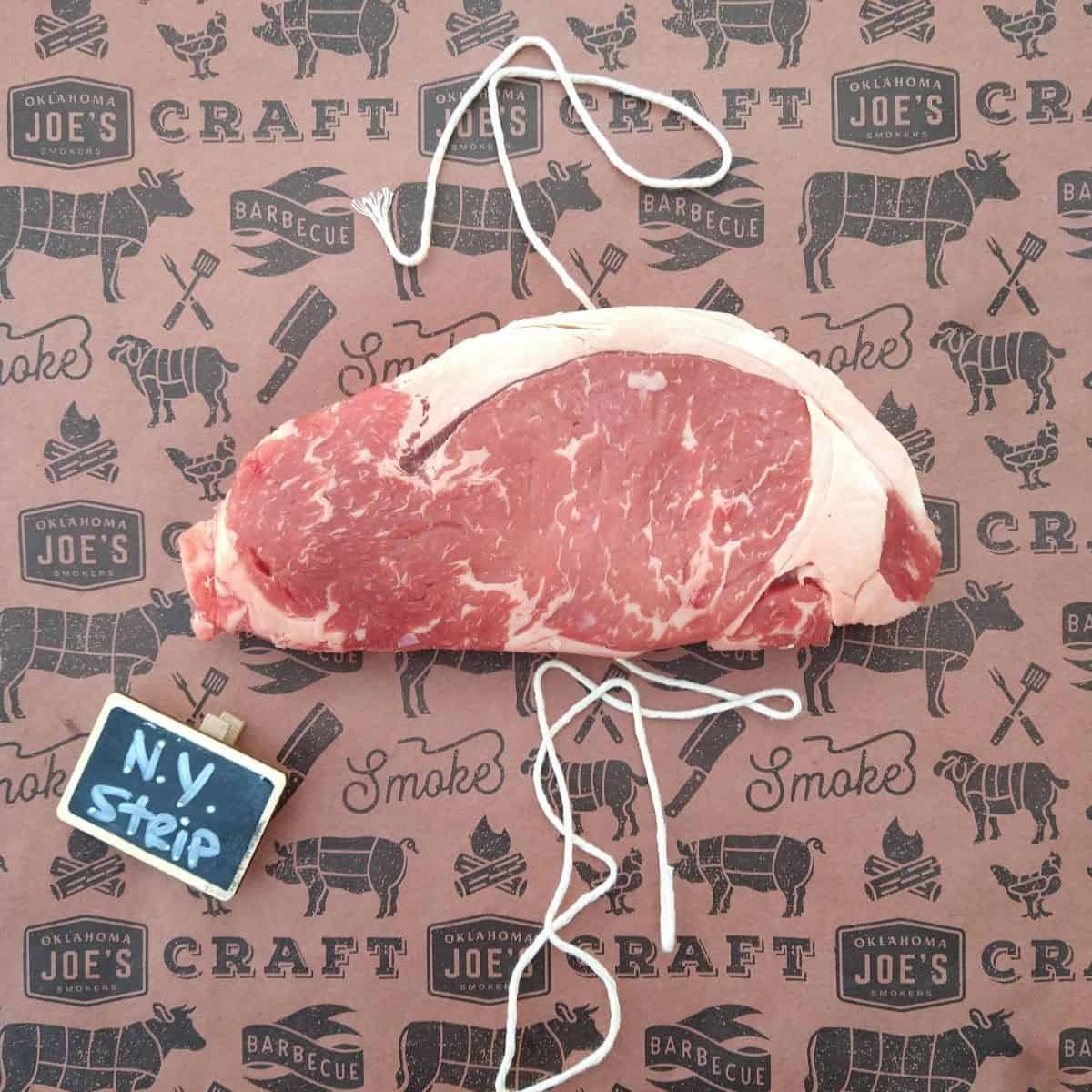 A raw New York strip steak on a piece of butcher paper with butcher string.