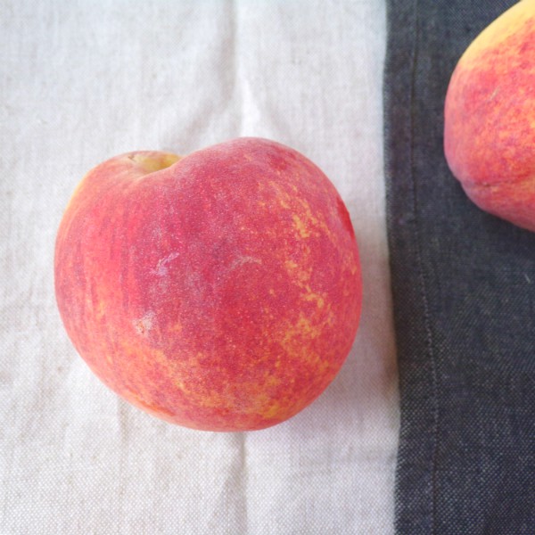 A single Flame Prince peach sitting on a white towel next to a single Flame Prince peach on a black towel