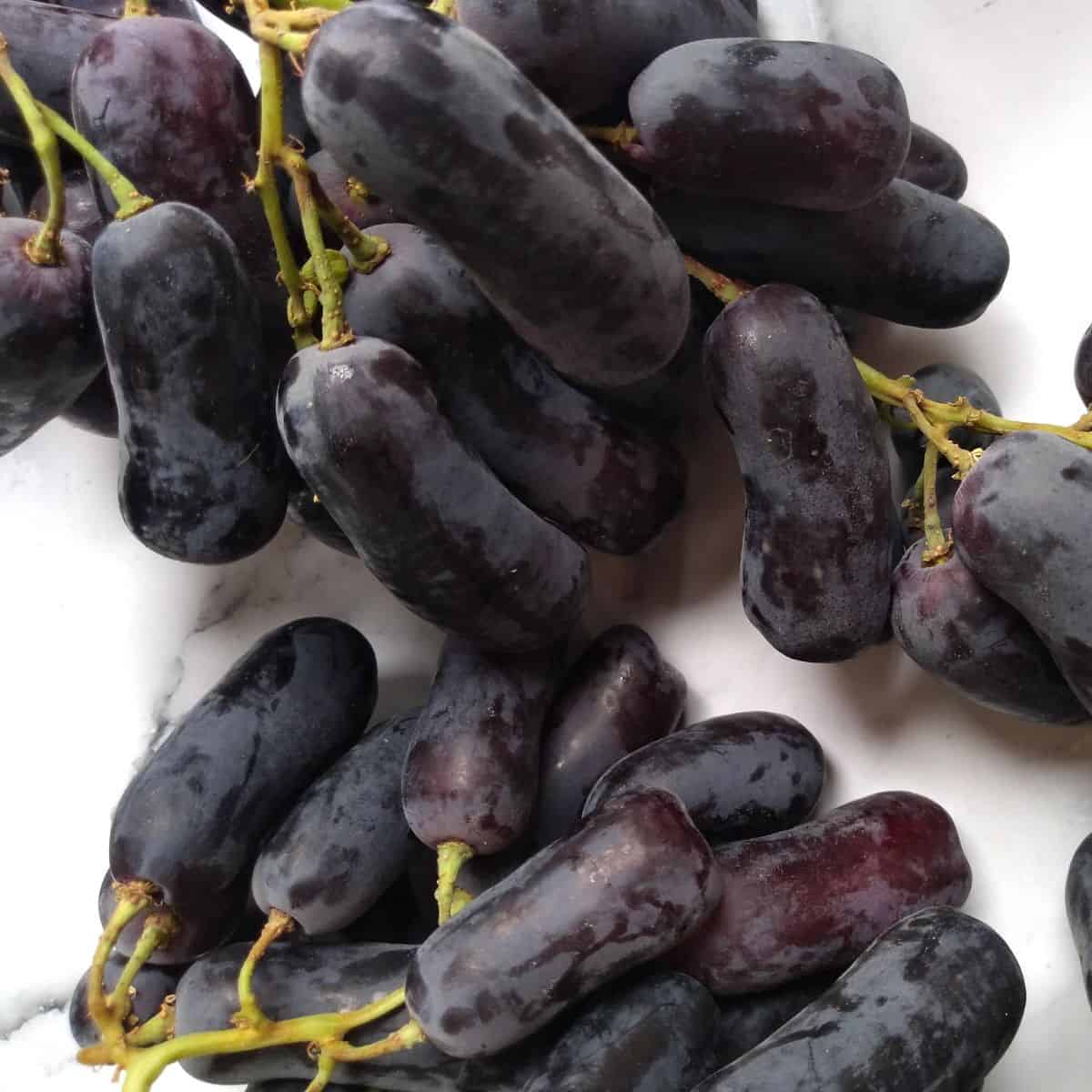 Elongated black Moon Drop grapes on a white board.