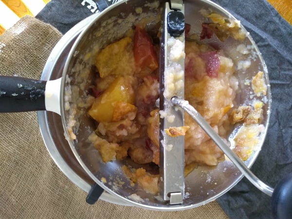 A food mill sitting on top of a pot with cooked apples ready to run through the food mill.