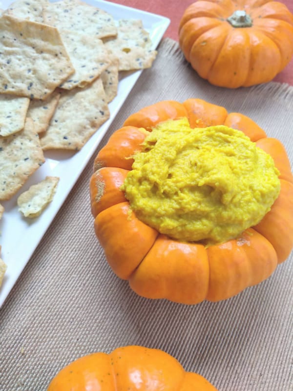 Fresh Pumpkin Hummus inside a in pumpkin with crackers on the left on a whiter plate.