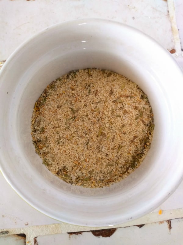 A white ramekin container filled with the herbs, salt, and spices from a brine mix. The container is on a white title countertop.