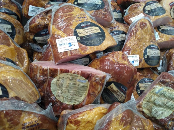 A display of Kirkland Master Carve half hams piled up at a Costco store.