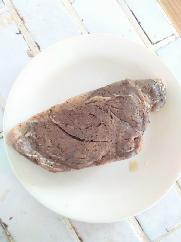 A finished sous vide chuck eye steak on a white plate before it has been seared.