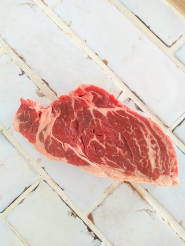 A Chuck Eye steak is sitting on a white tiled counter top.