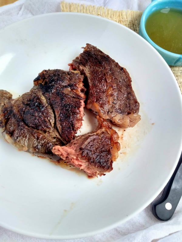 A cut open seared sous vide chuck eye steak on a white plate. You ca see lots of pink meat on the inside of the steak.