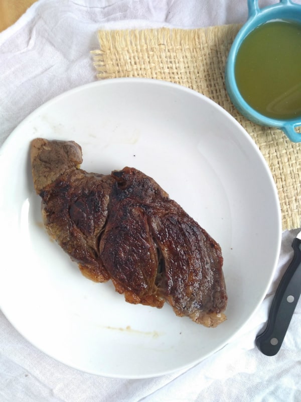 A cooked steak is on a white plate with a knife next to the plate.