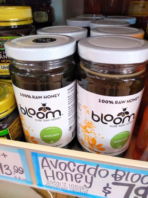 A grocery store display of 100% raw avocado blossom honey from Bloom honey in clear jars with a white lid and label.