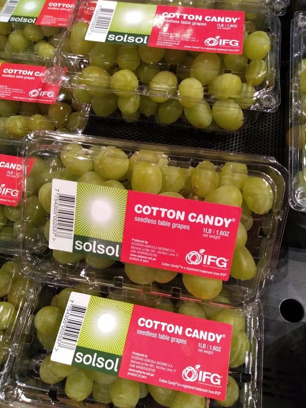 A display of Cotton Candy grapes in plastic clamshell containers.