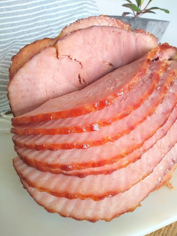 A spiral sliced ham on a white cutting board on a wood table with a gray striped towel in the background.