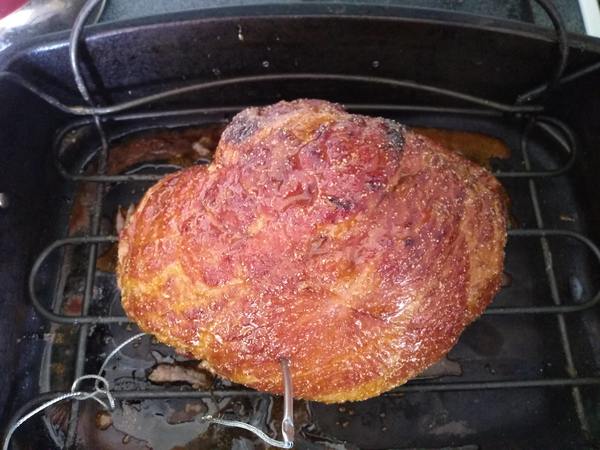 A glazed finished spiral ham in a large roasting pan with a wire rack with a probe stuck into it.