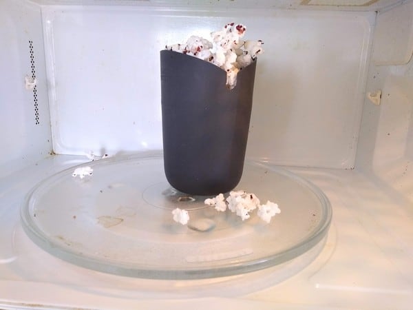 Joseph Joseph Single Serving Silicone Popcorn Maker in the microwave with popcorn spilling out.