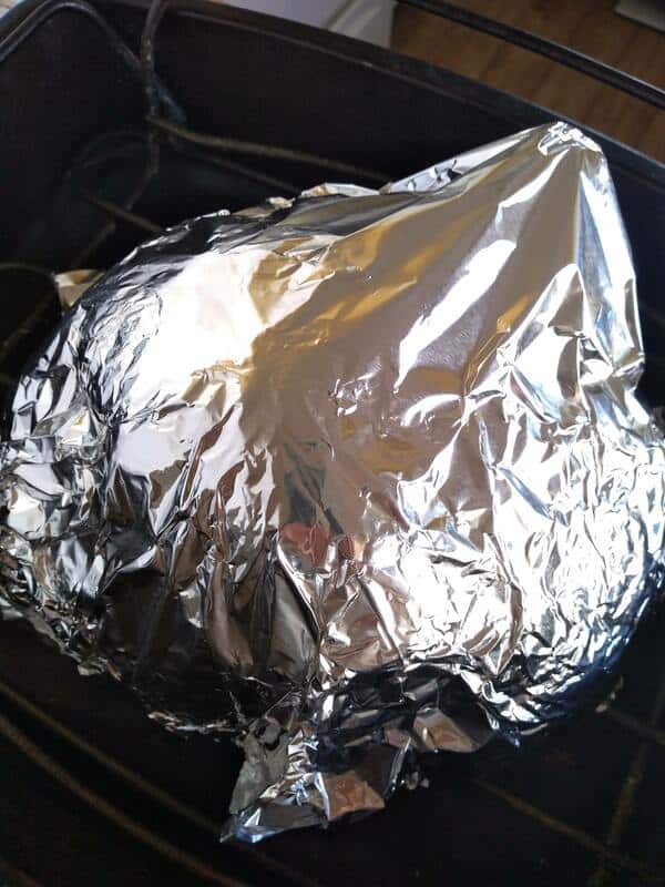 A spiral ham in a large roasting pan with a wire rack. The ham is covered with foil. 