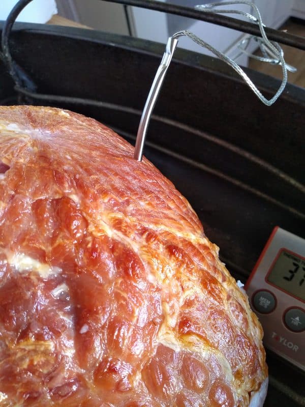 A spiral ham in a large roasting pan with a wire rack with the probe of a thermometer sticking into the ham.