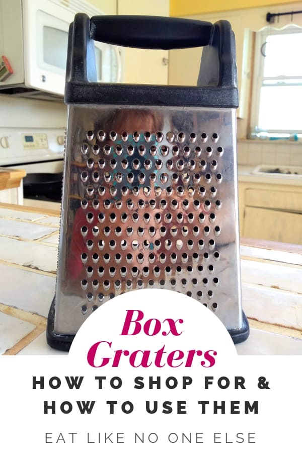 A box cheese grater that is metal with plastic bottom and handle on top sits on a white countertop in a kitchen. The words underneath it say "Box Graters How to Shop for & How to Use Them"