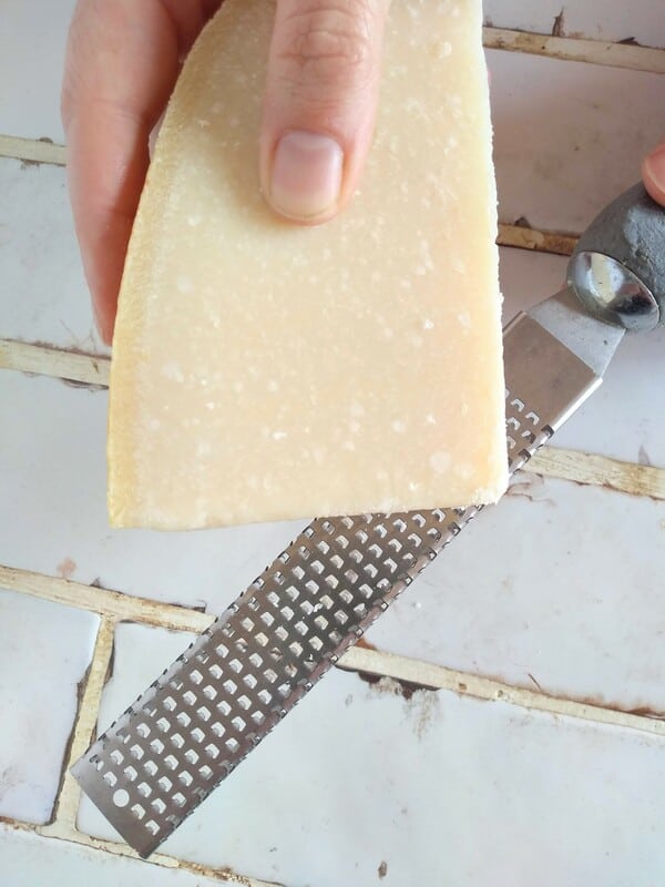 Grating parmesean cheese with Microplane grater on top of a white countertop