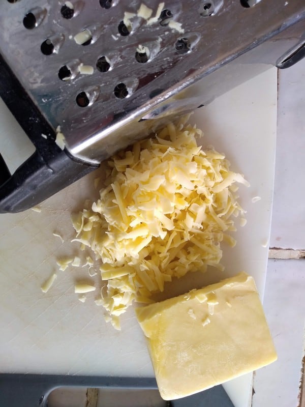 Shredded New Zealand cheddar cheese on a cutting board, next to a box grater.